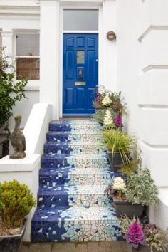 a blue door is on the side of a white house with flowers and plants in pots