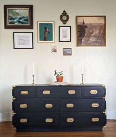 an old dresser is painted black with gold handles and brass pulls in front of pictures on the wall