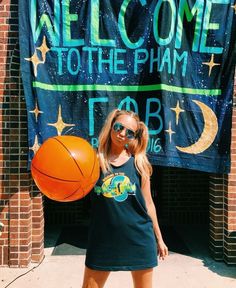 a woman holding a basketball standing in front of a welcome to the pham sign