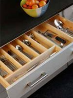 an open drawer with utensils and spoons in it next to a bowl of fruit