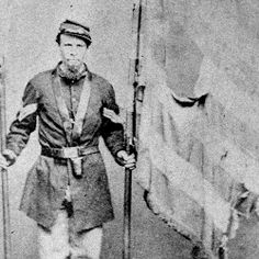 an old black and white photo of a man in uniform with skis standing next to two flags