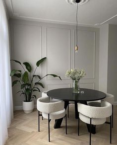a black table with four white chairs around it and a potted plant in the corner