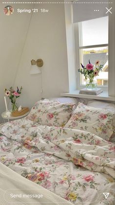 an unmade bed with flowers on it in front of a window next to a lamp