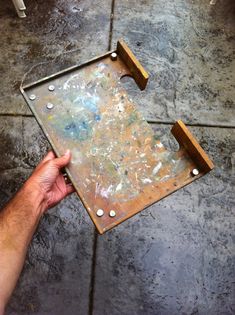 a hand holding a metal tray with holes in it on the ground next to a table