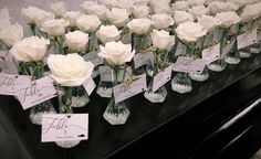 there are many white roses in vases on the table with name tags attached to them