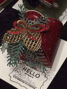 a red present wrapped in gold and green ribbon with a bow on it's top