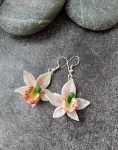 two pink flowers are hanging from silver earwires on some gray rocks with green beads