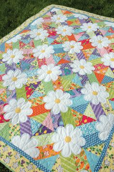 a quilt is laying on the grass in front of some green grass and one has white flowers