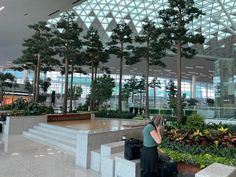 a woman sitting on top of a bench next to trees and plants in an airport