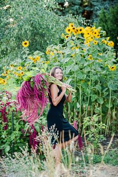 a woman in a black dress is holding a large bundle of plants and smiling at the camera