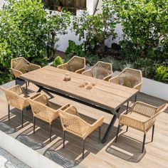 an outdoor dining table and chairs on a wooden deck with plants in the back ground