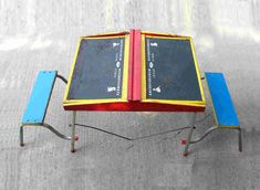 an open book sitting on top of a table with two benches underneath it and one bench below