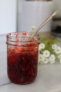 a glass jar filled with jam sitting on top of a counter next to white flowers