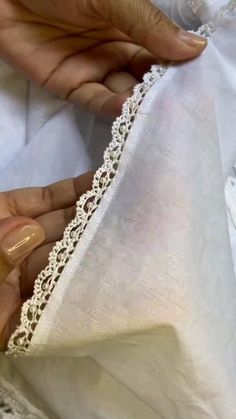 two hands are stitching the edge of a white dress with lace on it and another hand is holding an object