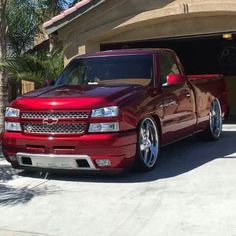 a red truck is parked in front of a garage with palm trees and a house behind it