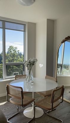 a dining room table with four chairs and a vase on the table in front of two large windows