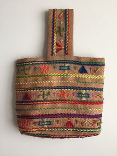 a woven bag hanging on the wall with colorful trimmings and beads around it