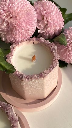 a pink candle sitting on top of a plate next to flowers