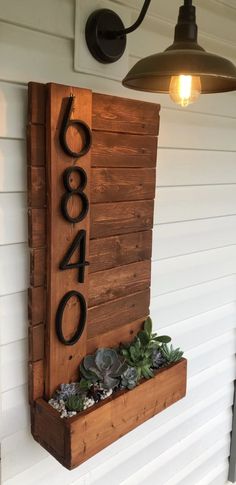 a wooden house number sign with succulents and plants in the planter