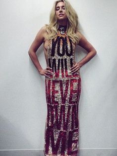a woman standing in front of a white wall wearing a red and gold dress with words written on it