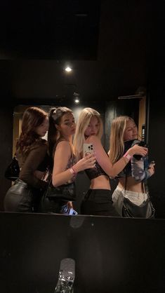 three beautiful young women standing in front of a mirror looking at their cell phones and taking pictures