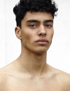 a close up of a person with no shirt on and black curly hair in front of a white wall
