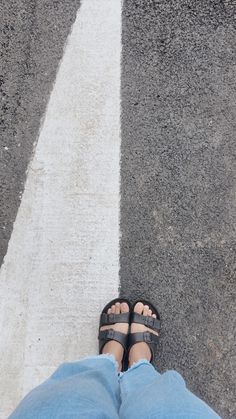 a person wearing sandals standing in the middle of an empty road with their feet crossed