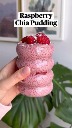 a person holding up a raspberry chia pudding in front of a plant