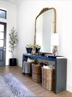 a large mirror sitting above a blue table with baskets on top of it next to a lamp