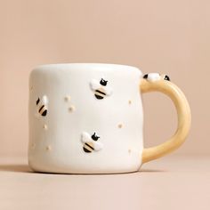 a ceramic mug with bees on it sitting on a table next to a wall and a pink background