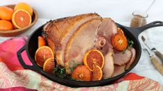 a roasting pan filled with ham, oranges and other food on top of a table