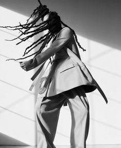 a man with dreadlocks standing in front of a white wall wearing a suit