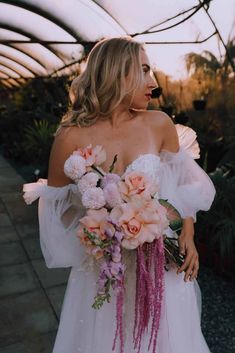 a woman in a white dress holding a pink and purple flower bouquet on her wedding day