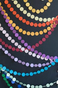 multicolored paper circles are arranged on a black background with string lights hanging from the ceiling