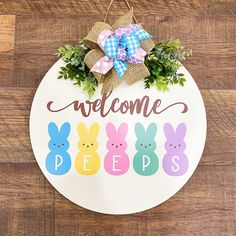 a welcome sign hanging on the side of a wooden wall with bunnies and greenery