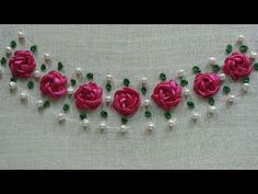 some pink flowers and pearls are on a white cloth with green bead trimmings