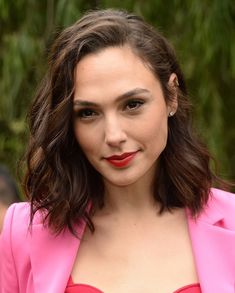 a close up of a person wearing a pink suit and red lipstick with trees in the background