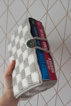 a hand is holding two books on top of a crocheted book holder with scissors in it