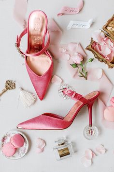 pink high heeled shoes and accessories laid out on a white surface with rose petals