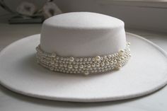 a white hat with pearls on it sitting on top of a table next to a window