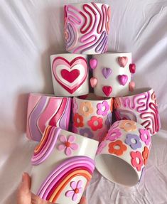 a hand is holding several colorful cups with hearts and flowers on them