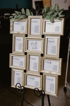 a table with many framed pictures and greenery on it's stand, as well as the names of each guest
