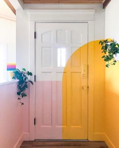 the door is painted pink, yellow and white with a plant in front of it