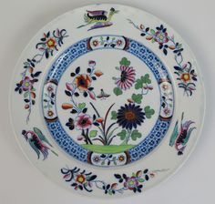 a plate with flowers and birds painted on the front, sitting on a white surface