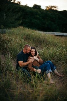 a man and woman are sitting in the grass with their arms around each other as they smile