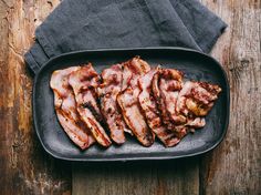 sliced bacon in a black dish on a wooden table next to a gray towel and napkin