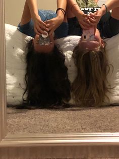 two people laying on top of a bed in front of a mirror with their feet up