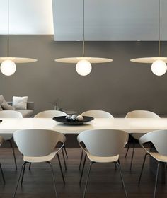 a dining room table with white chairs and hanging lights