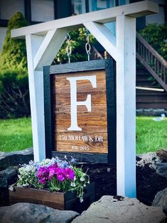 a wooden sign with the letter f on it and flowers growing in front of it