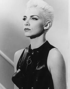 a black and white photo of a woman with short hair wearing a leather dress, looking off to the side